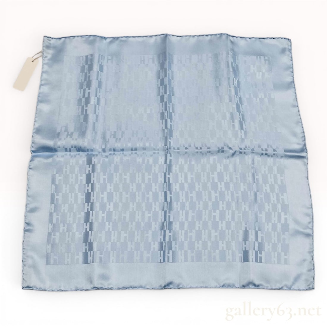 Hermes Faconnee H Light Blue Silk Pocket Square with tags w/Box: An Hermès pocket square crafted from light blue silk featuring the Façonnée H pattern, a tone-on-tone jacquard-woven repeating H logo motif. The fabric displays the woven mark HER