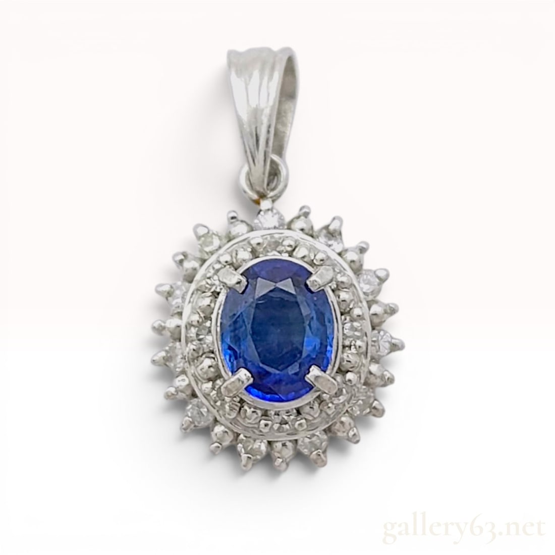 18K White Gold Natural Sapphire and Diamond Double Halo Pendant: An 18 karat white gold gemstone cluster pendant featuring a central oval-faceted natural blue sapphire. The sapphire is bordered by two tiered concentric halos of prong-set round brilliant-cut diamond