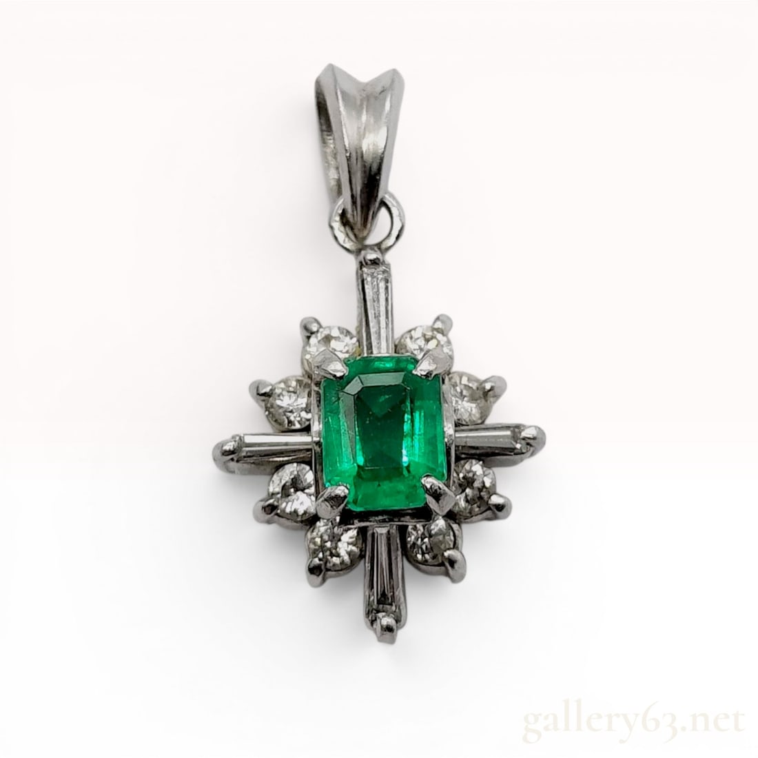 Platinum Emerald and Diamond Cluster Pendant: This platinum pendant features a central rectangular step-cut green emerald held in a corner-prong setting. The emerald is framed by a tiered cluster of twelve diamonds in a starburst configuration, c