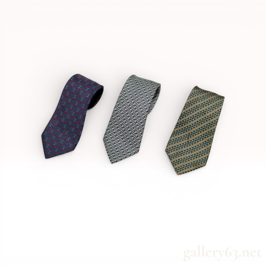 Three Hermes Silk Printed Neckties: This lot consists of three designer neckties from Herm?¨s, Paris, each made in France from 100 percent silk. The collection features various repeating geometric and equestrian-inspired patterns chara