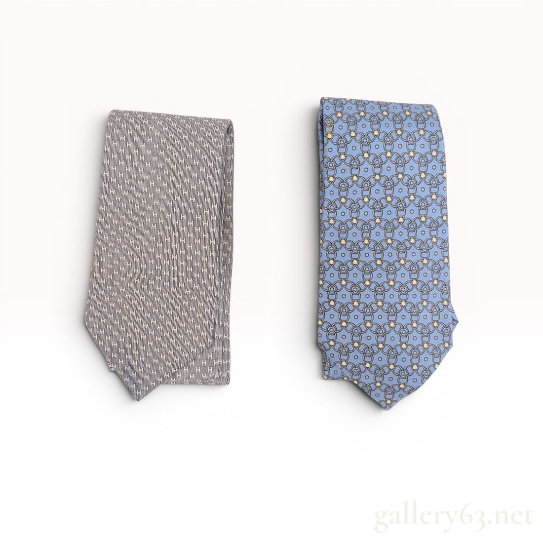 Two Designer Silk Neckties, Including Hermes H Monogram: Two silk neckties featuring repetitive geometric patterns in shades of blue and white. The first tie is by Hermès and features a navy blue H monogram pattern on a white ground, while the second