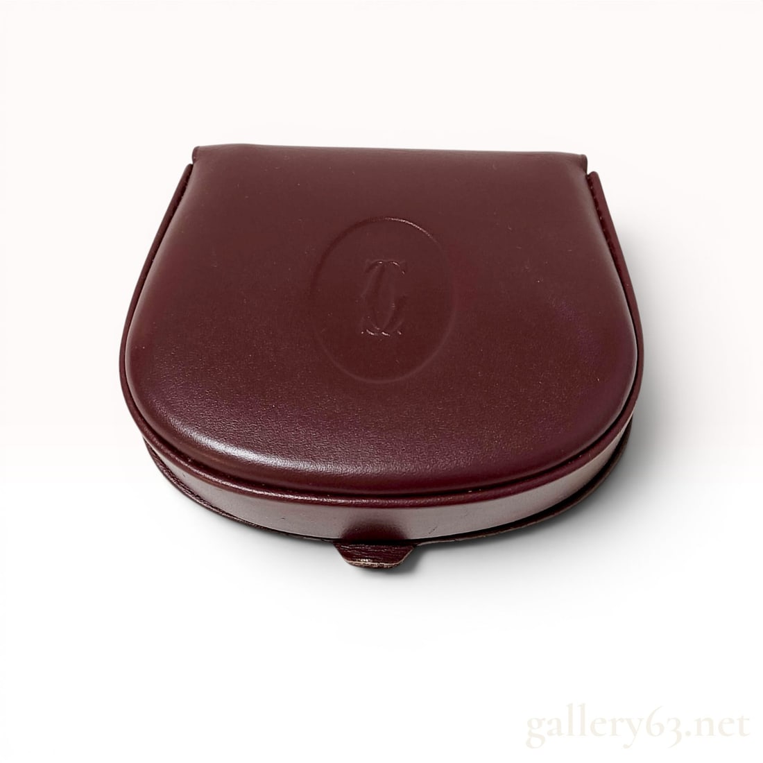 Cartier Must de Cartier Burgundy Leather Horseshoe Coin Purse: Cartier Must de Cartier burgundy leather coin purse in a structured horseshoe silhouette. The design features a flap closure with an embossed interlocking logo medallion and tonal stitching throughout