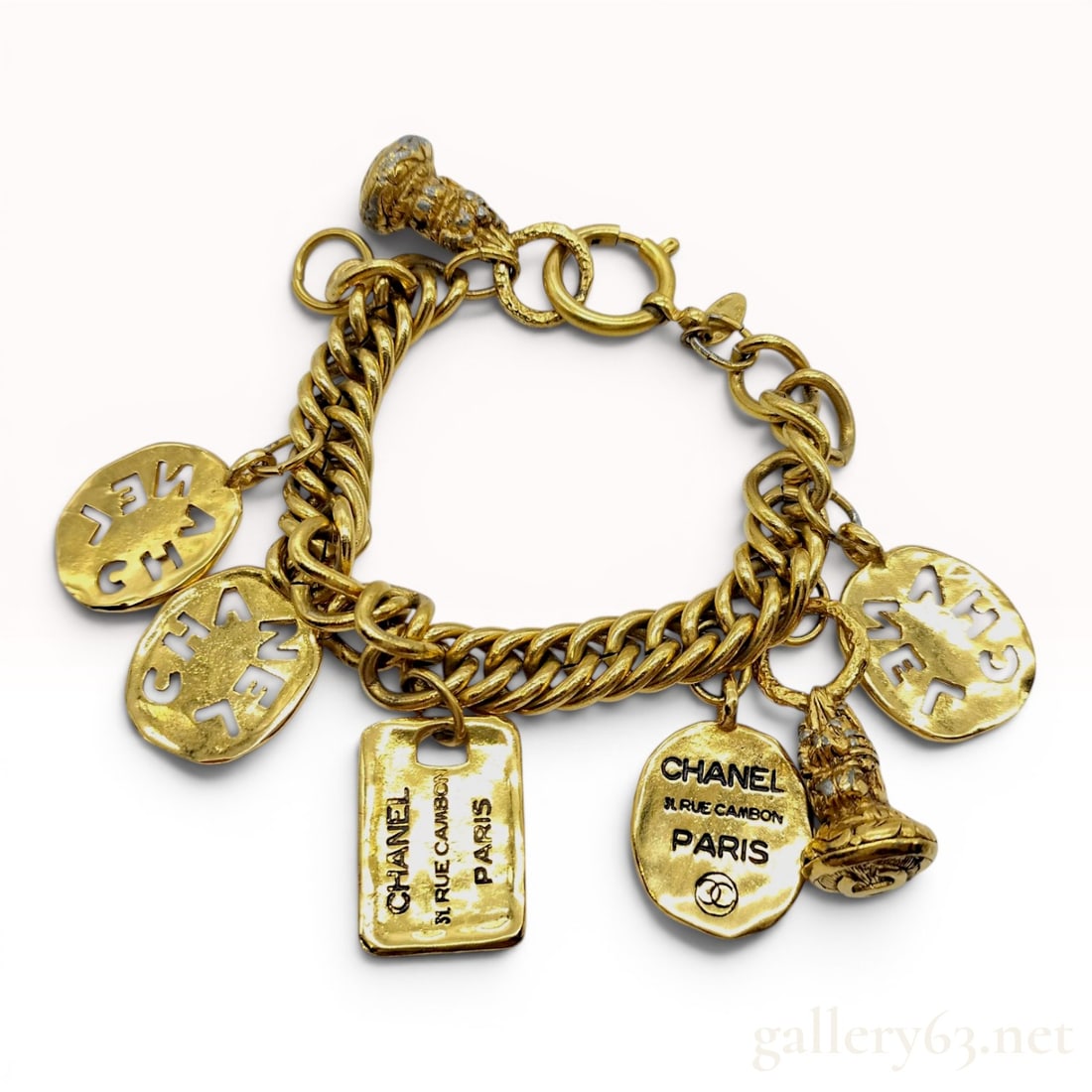 Rare Chanel Vintage Gold-Plated Rue Cambon Charm Bracelet: A vintage Chanel charm bracelet featuring a heavy curb link chain in heavy gold plate. The bracelet is adorned with seven distinct charms including three circular openwork charms with cutout CHANEL le