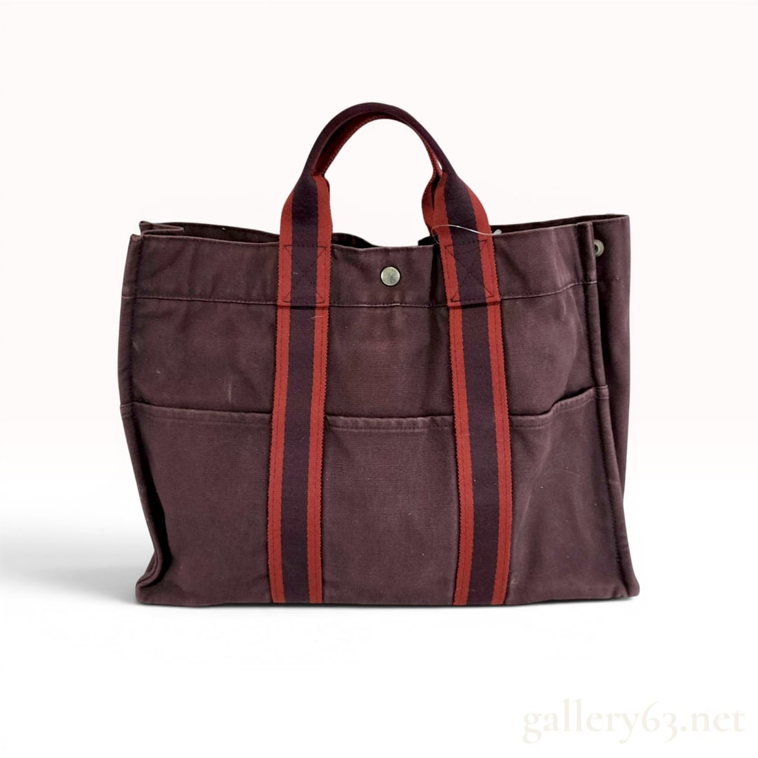 Hermes Fourre Tout GM Canvas Tote Bag: This Hermes Fourre Tout GM tote bag is constructed from maroon cotton canvas featuring signature striped webbing handles in red and maroon. The exterior design incorporates three slip pockets on both 