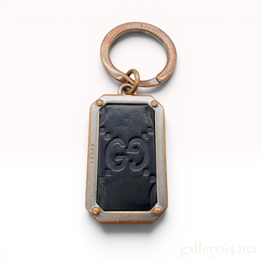 Gucci Guccissima Leather and Metal Keychain: This authentic Gucci keychain features a rectangular metal tag with a dark brown or black leather inlay. The leather is debossed with the signature interlocking GG Guccissima pattern and geometric acc