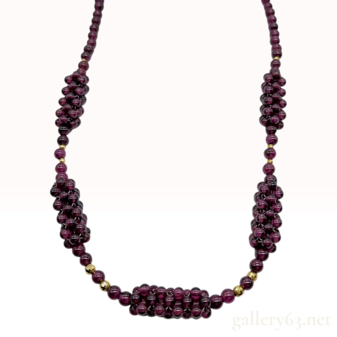 18K Yellow Gold and Tourmaline Beaded Cluster Necklace: A beaded necklace composed of polished round tourmaline beads and 18K yellow gold components. The design features single-strand sections of garnet beads alternating with five cylindrical woven bead cl