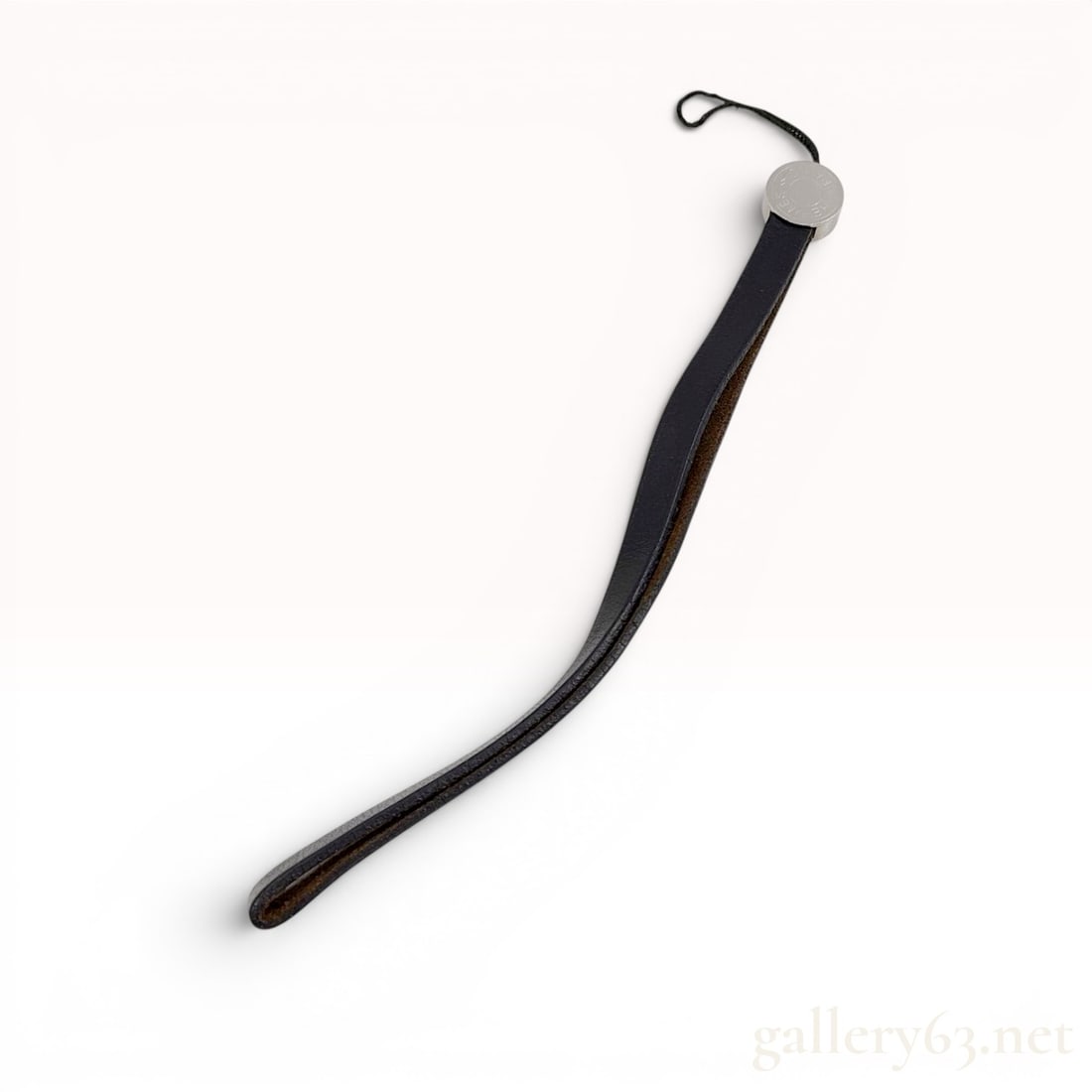 Hermes Black Leather and Silver-Toned Clou de Selle Wrist Strap: A black leather wrist strap for a mobile phone or camera by Hermes, Paris. The accessory features a length of folded black leather secured by a circular, silver-toned metal cap in the signature Clou d