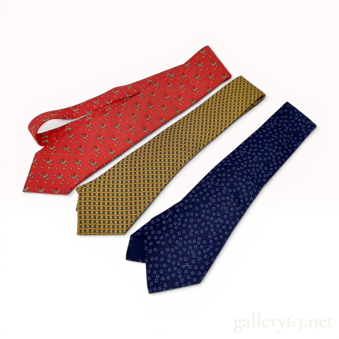 A Trio of Hermes Silk Neckties: This lot consists of a trio of designer silk neckties from Hermes, Paris. The collection features three distinct patterns: a red tie with a whimsical repeating pattern of figures in green attire ice f