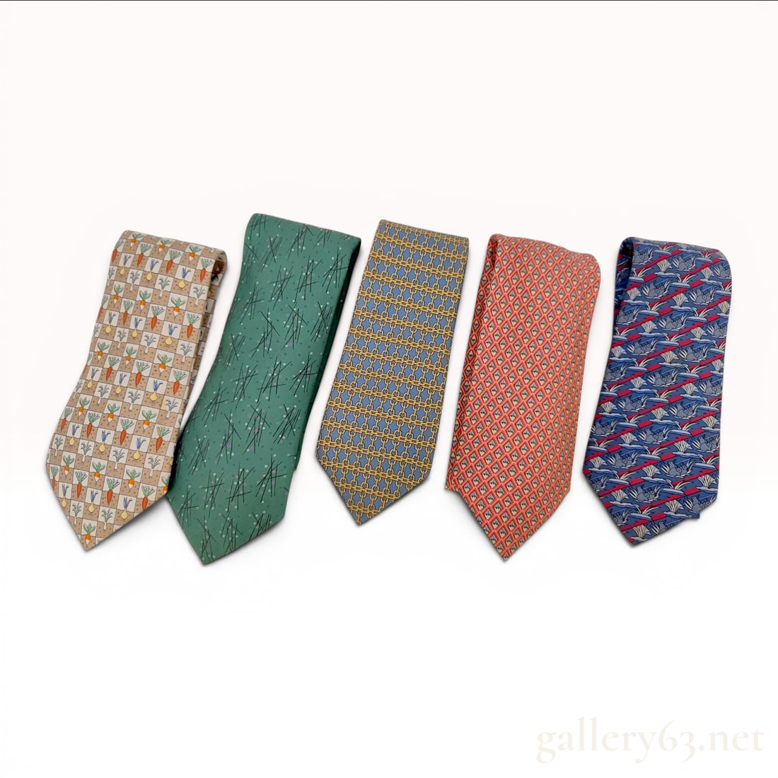 A Lot of Five Designer Silk Neckties, Including Hermes: A collection of five designer silk neckties, primarily consisting of pieces by Hermes Paris. The assortment features a variety of signature patterns and colors. Included is a navy blue Hermes tie with