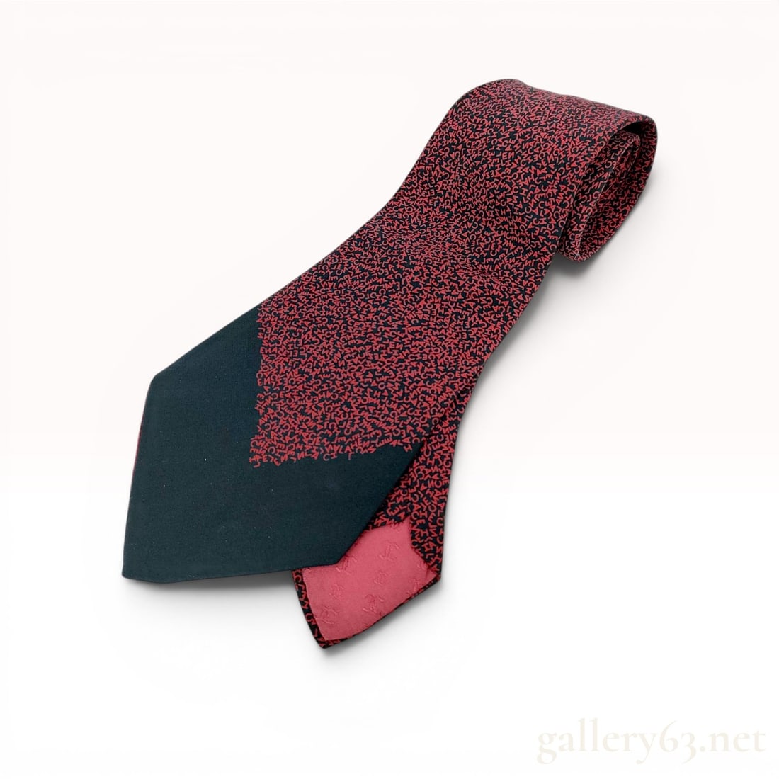 Chanel Typographic Logo Print Silk Necktie: A silk necktie by Chanel featuring a dense typographic logo print. The pattern consists of jumbled red letters spelling CHANEL across a black ground. The wide blade is finished with a solid black colo