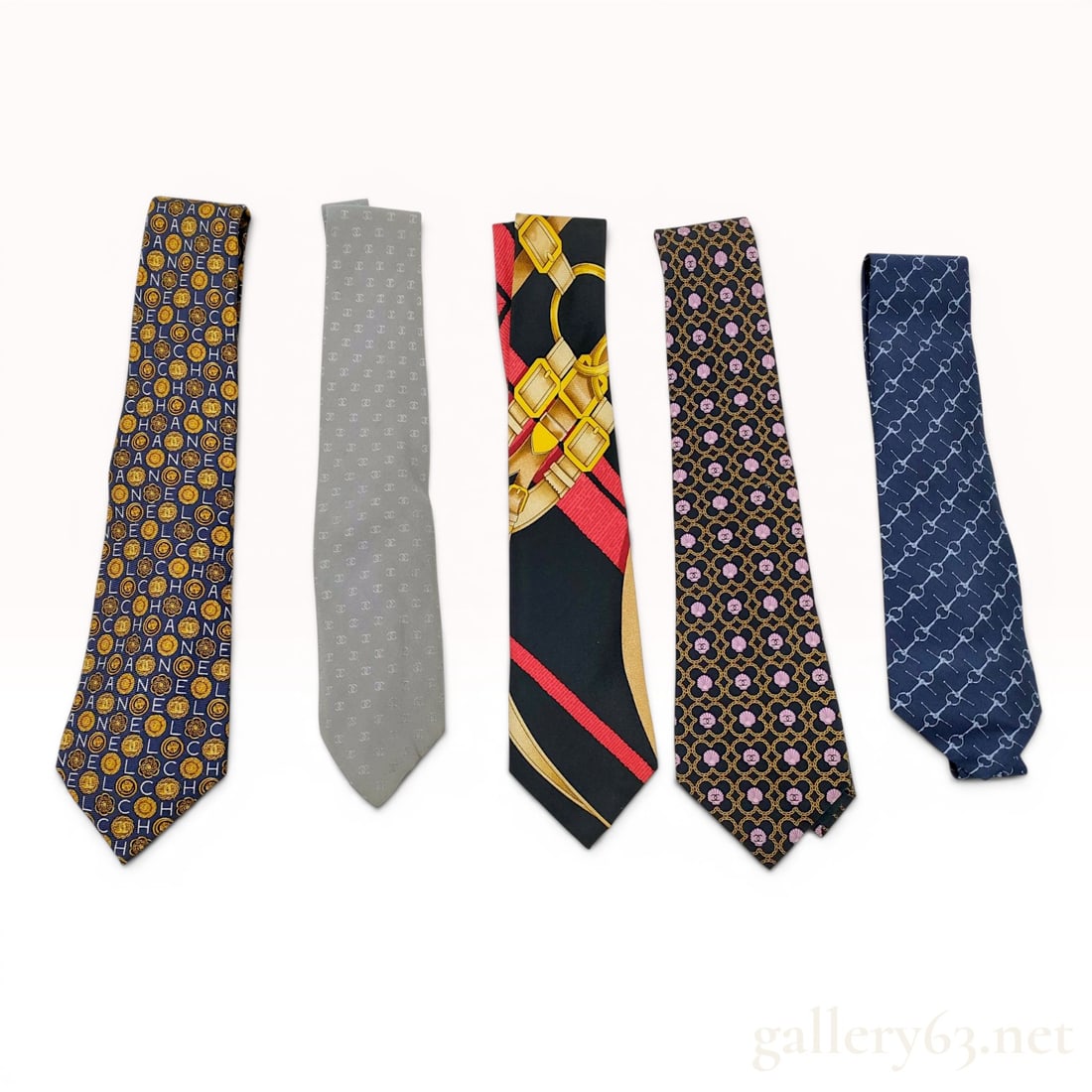 A Collection of Five Designer Silk Neckties Including Chanel and Hermes: This lot features five designer silk neckties from prominent fashion houses, including Chanel and Hermes. The collection includes a Chanel navy blue silk tie with a repeating pattern of gold-tone inte
