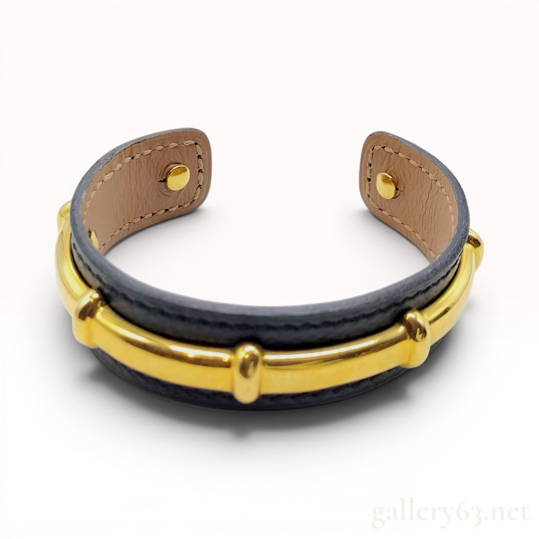 Hermes Leather and Gold-Toned Metal Bamboo Motif Cuff Bracelet with Box: An Hermes cuff bracelet featuring a black leather exterior and a tan leather interior. The band is accented with a polished gold-toned metal bar detailed with three raised vertical bands, a design ele