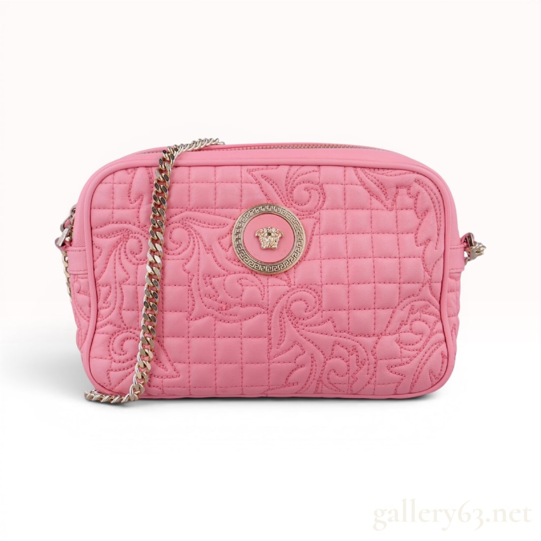 Versace Pink Quilted Barocco Leather Camera Bag: This Versace camera bag is crafted from pink leather featuring an intricate quilted Barocco scroll pattern set against a grid-quilted background. The rectangular bag is secured with a top zip closure 