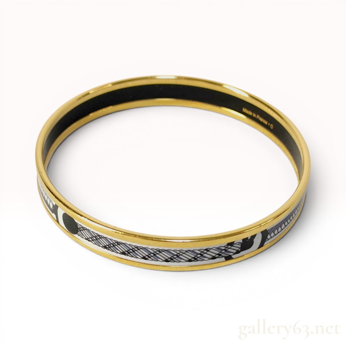 Hermes Enamel and Gold-Plated Narrow Bangle Bracelet: A narrow enamel bangle bracelet by Hermes featuring a gold-plated metal frame. The printed enamel exterior depicts a stylized braided rope or whip motif in shades of white, gray, and black. The interi