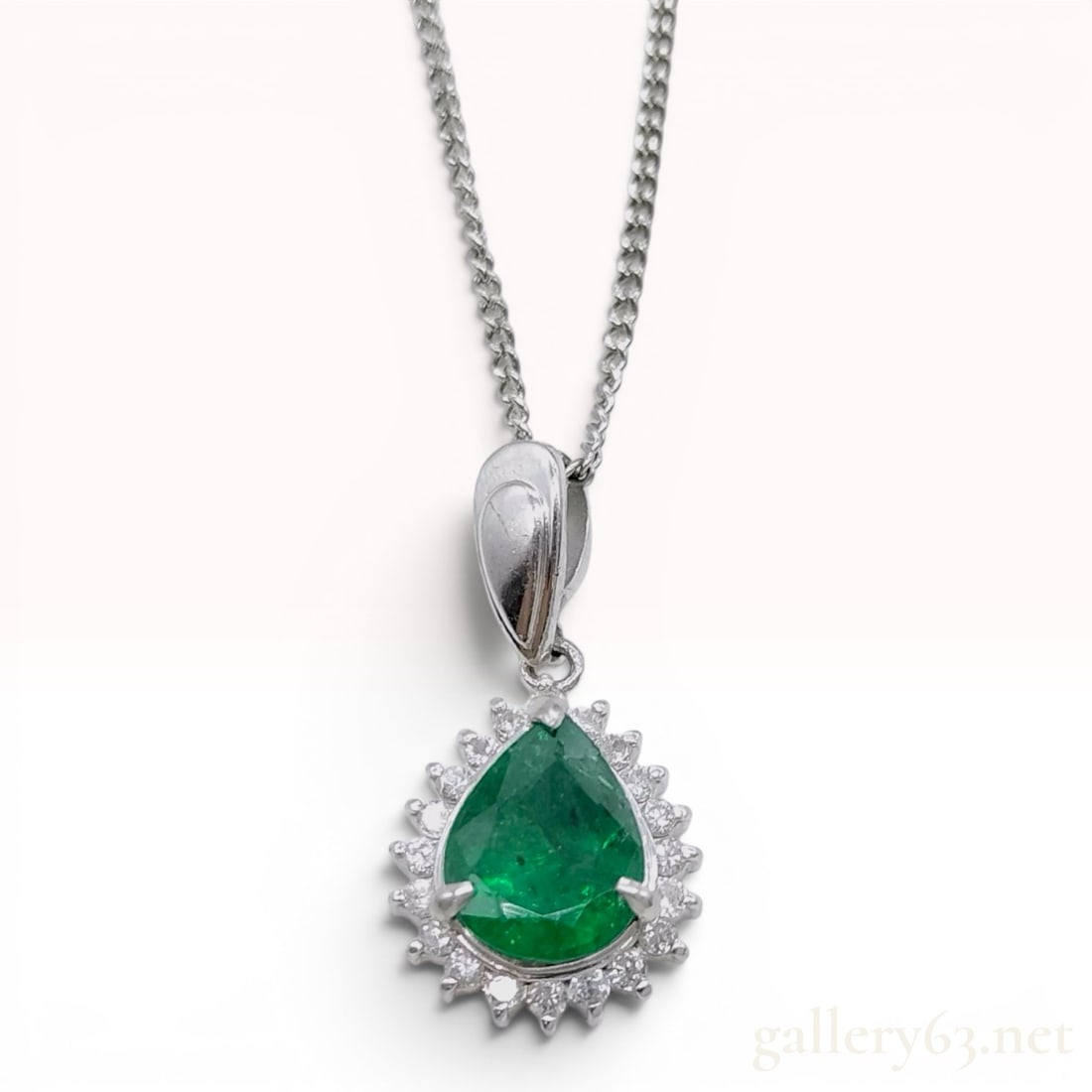 Platinum Emerald and Diamond Halo Pendant Necklace: This platinum necklace features a pendant set with a pear-cut green emerald weighing 0.97 carats. The center stone is secured in a three-prong setting and exhibits visible internal and surface-reachin