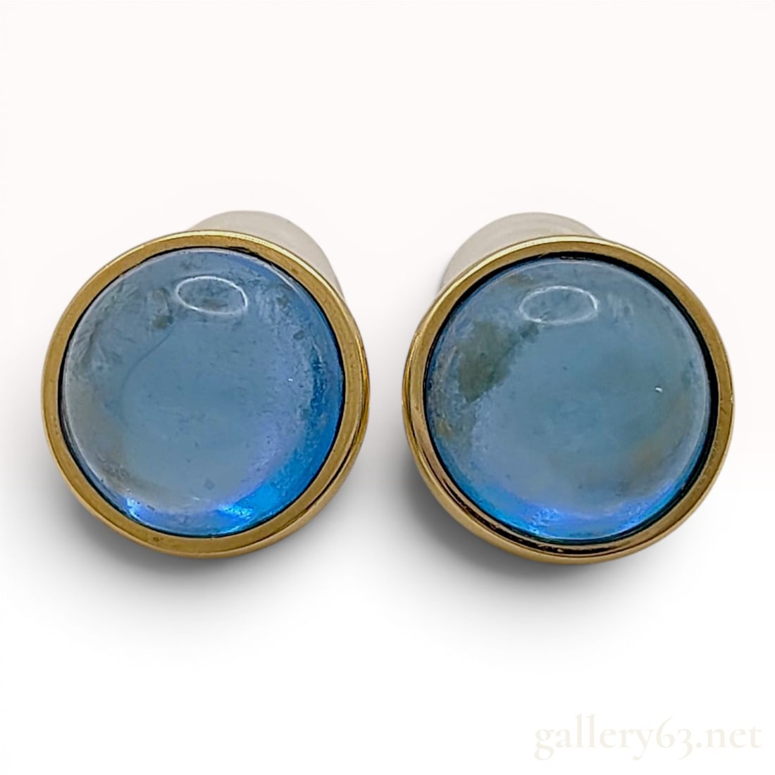 A Pair of 18K Yellow Gold and Blue Topaz Cabochon Stud Earrings in the style of Tiffany & Co: A matched pair of 18k yellow gold stud earrings in the style of Tiffany & Co. Featuring round, vibrant blue cabochon-cut blue topaz, bezel-set in polished 18K yellow gold. Each earring post is stamped