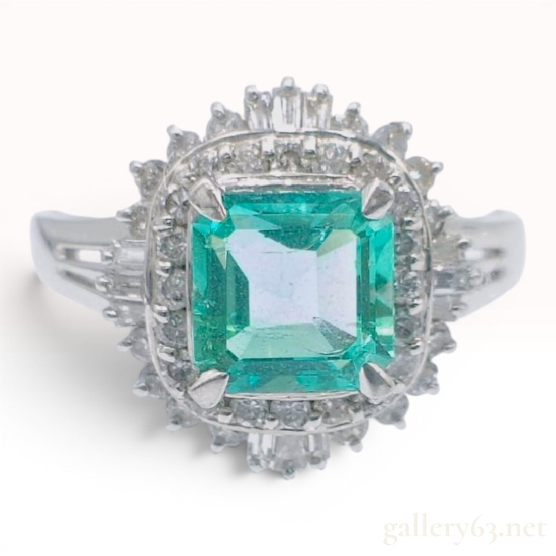 Platinum Emerald and Diamond Ballerina Style Cocktail Ring: This cocktail ring is crafted in platinum and features a central emerald-cut emerald. The emerald is secured by four prongs within a tiered ballerina style halo. The inner tier consists of small round