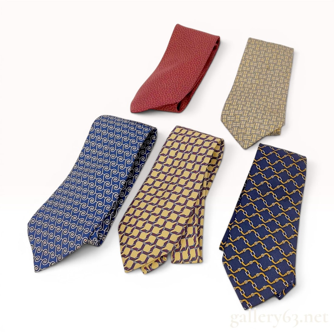 A Group of Five Hermes Silk Neckties: A group of five silk neckties produced by Hermes, Paris. Each tie is crafted from 100 percent silk twill and features a distinct repeating pattern. The collection includes a navy blue tie with a gold-