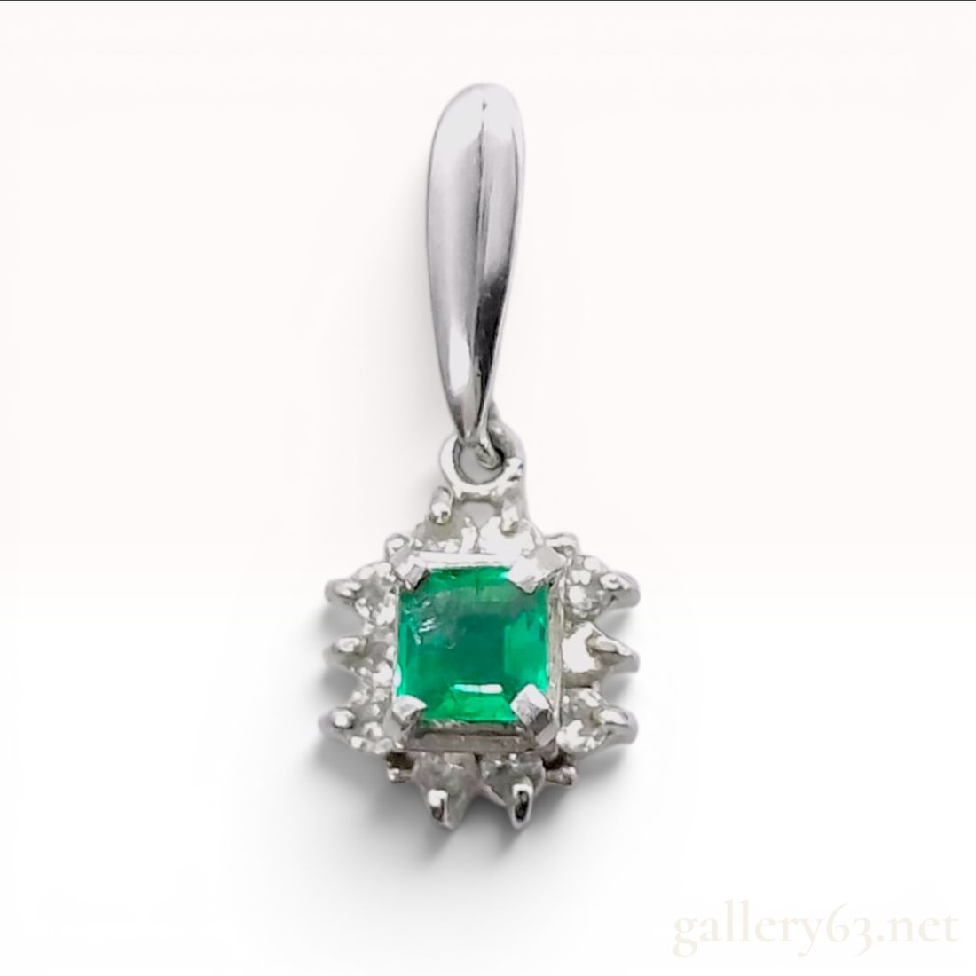 Estate Platinum Emerald and Diamond Halo Pendant: A platinum pendant featuring a central square emerald-cut green emerald weighing approximately 0.14 carats. The emerald is secured by four corner prongs and is encircled by a halo of ten round brillia