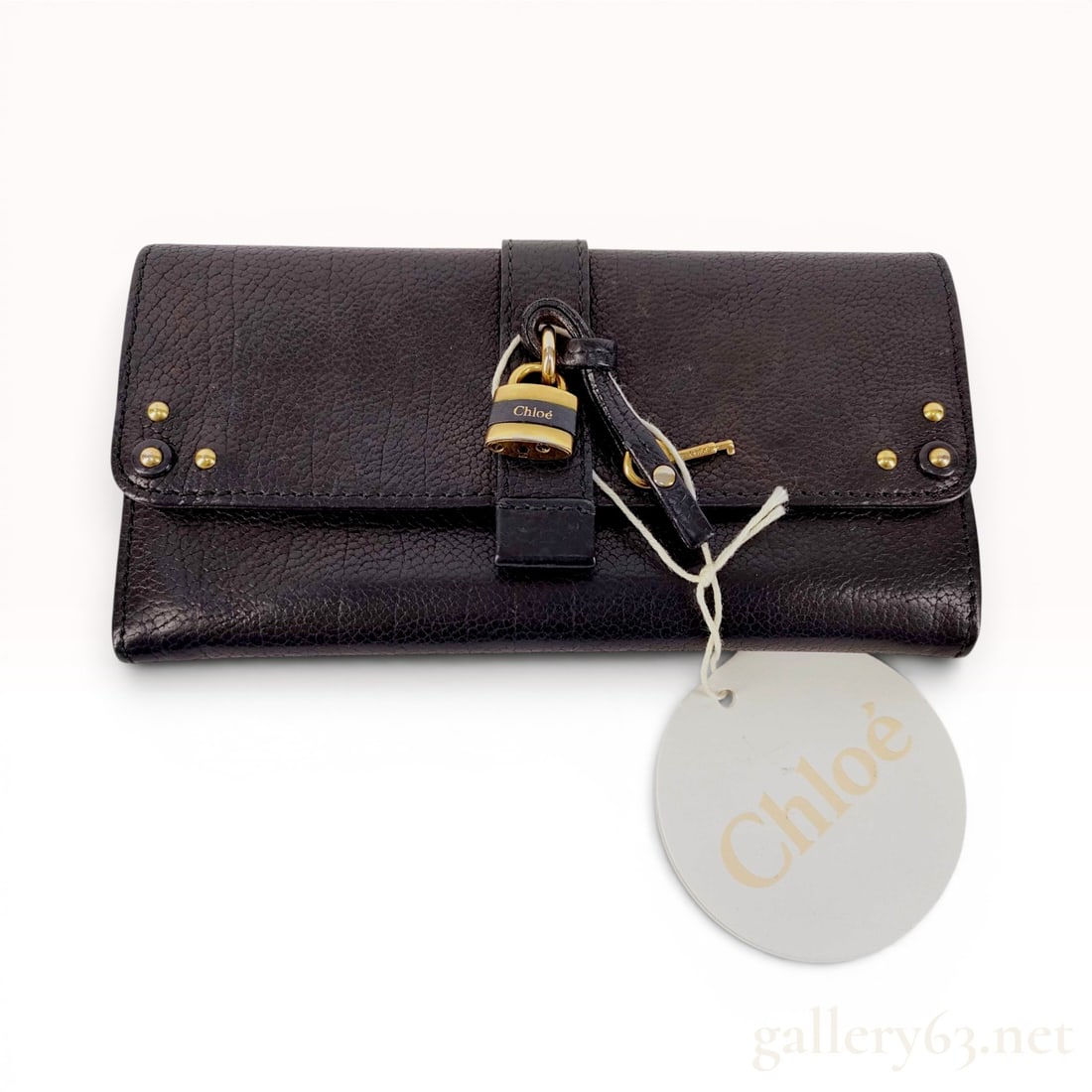 Chloe Paddington Black Pebbled Leather Long Wallet: This Chloe Paddington long wallet is constructed from black pebbled leather with gold-tone brass hardware. The design features a tri-fold rectangular silhouette with a decorative wrap-around leather s