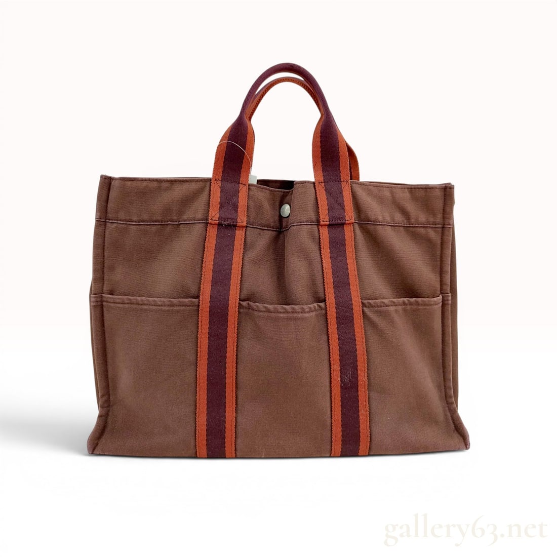 Hermes Fourre Tout MM Canvas Tote Bag: An Hermes Fourre Tout MM tote bag crafted from chocolate brown canvas. This utilitarian design features double top handles made of bicolor burgundy and orange canvas webbing, which continue as vertica