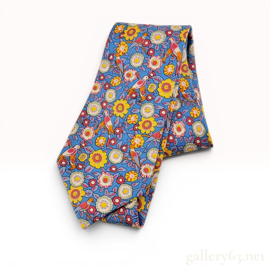 Hermes Silk Twill Necktie with Parrot and Floral Motif with Box: This Hermes necktie is crafted from 100 percent silk and features a detailed print of multi-colored parrots perched among stylized floral and leaf motifs. The design is set against a medium blue groun