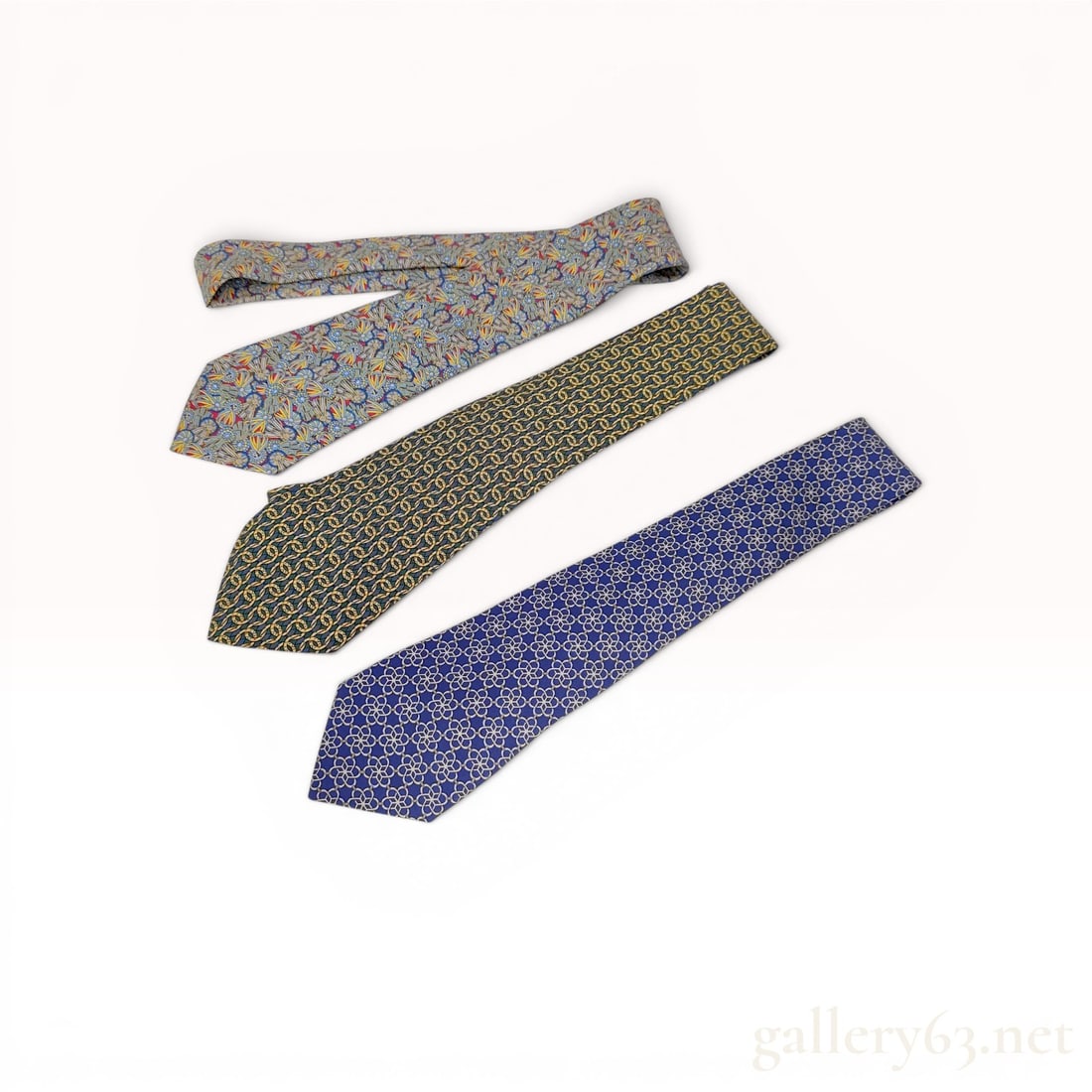 Group of Three Hermes Silk Neckties: A collection of three 100% silk neckties by Hermes, Paris. Each tie features a signature repeating pattern and hand-finished construction on a silk twill base. The first tie displays a dense, multi-co