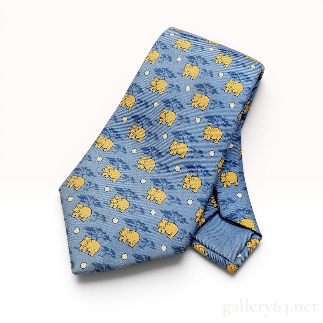 Hermes Safari Printed Silk Tie with Hippo Motif: An Hermes printed silk necktie featuring a savanna-inspired pattern with a repeating motif of yellow hippopotamuses, dark blue trees, and cream-colored dots on a light blue ground. The reverse of the 