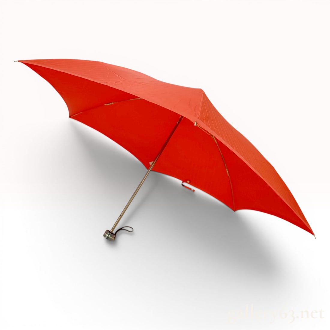 Yves Saint Laurent Red Tonal Monogram Jacquard Folding Umbrella: This is a designer folding umbrella by Yves Saint Laurent featuring a vibrant red canopy. The canopy is constructed from a synthetic fabric with a tonal jacquard-woven YSL monogram pattern. The umbrel