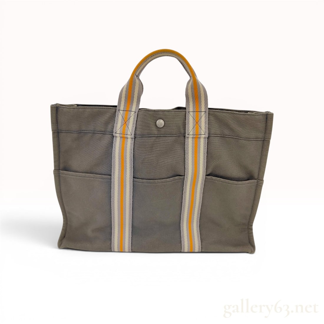 Hermes Fourre-Tout GM Gray Canvas Tote Bag: This Hermes Fourre-Tout GM tote bag is constructed from heavy-duty gray toile canvas. The rectangular silhouette features signature vertical striped webbing handles in gray, cream, and orange that enc