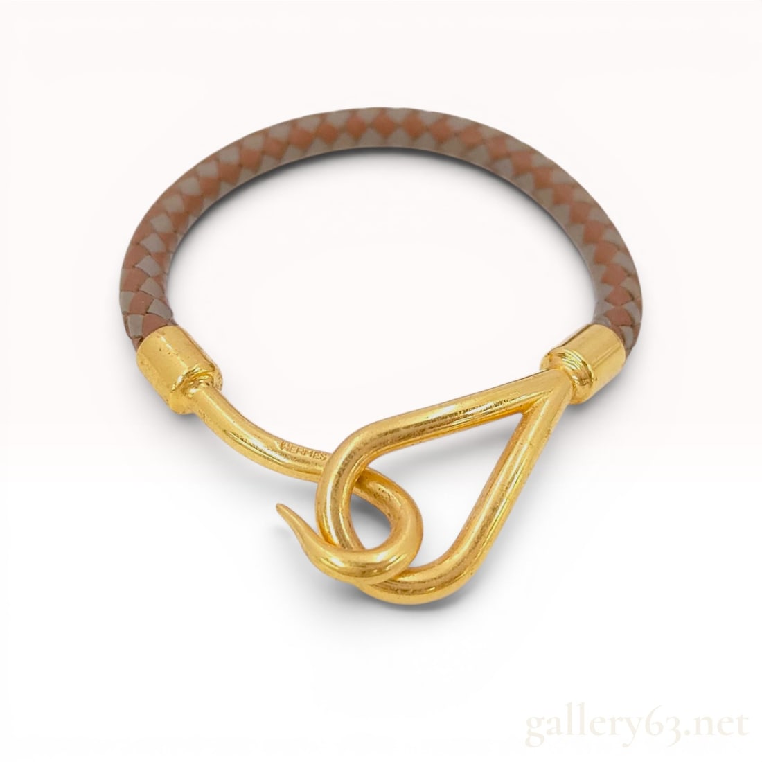 Hermes Jumbo Hook Gold-Plated Woven Leather Bracelet: This Hermes Jumbo style bracelet features a round, two-tone woven leather cord in shades of reddish-brown and taupe-grey. The piece is secured with yellow gold-tone metal hardware consisting of a styl