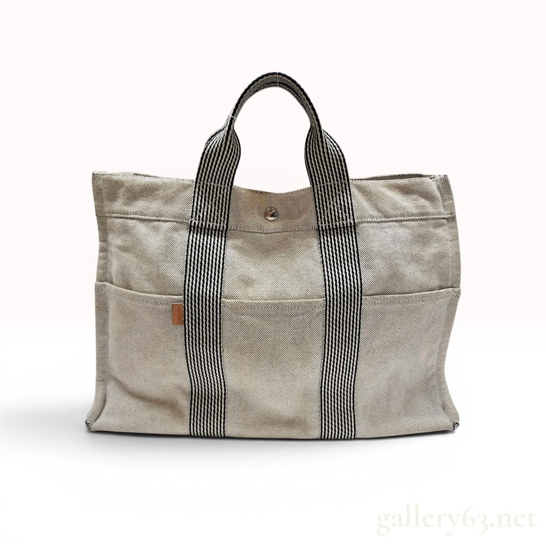 Large Hermes Fourre-Tout Canvas Tote Bag: Large Hermes Fourre-Tout tote bag crafted from a woven cotton canvas in a neutral grey and tan colorway. The bag features double top handles made of vertically striped black and cream webbing that ext