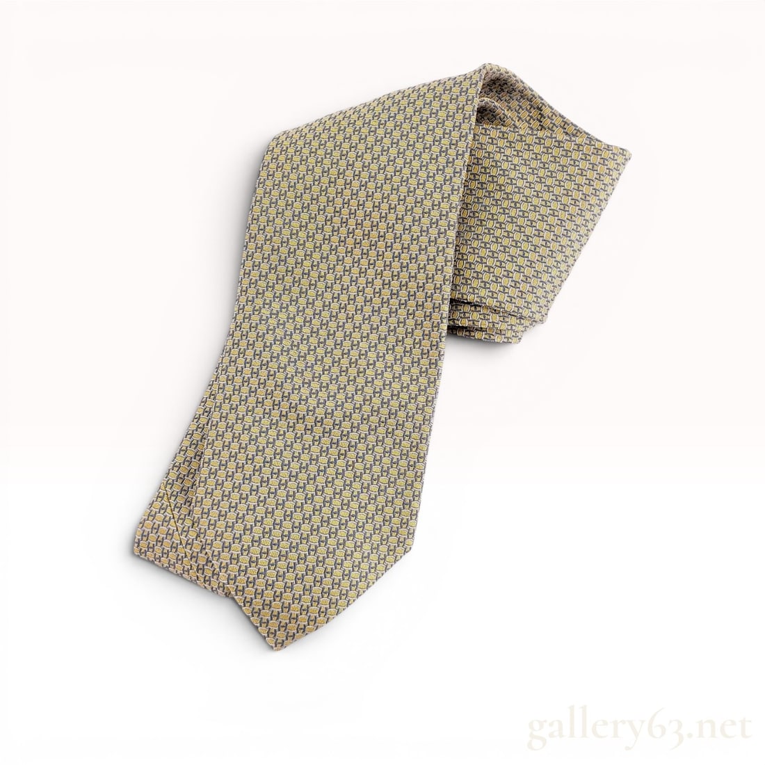 Hermes Silk Necktie Model 659128T: A 100 percent silk necktie by Hermes, Paris. The tie features a repeating geometric pattern of yellow H motifs and grey-blue chain link elements. It is constructed with a black silk lining woven with