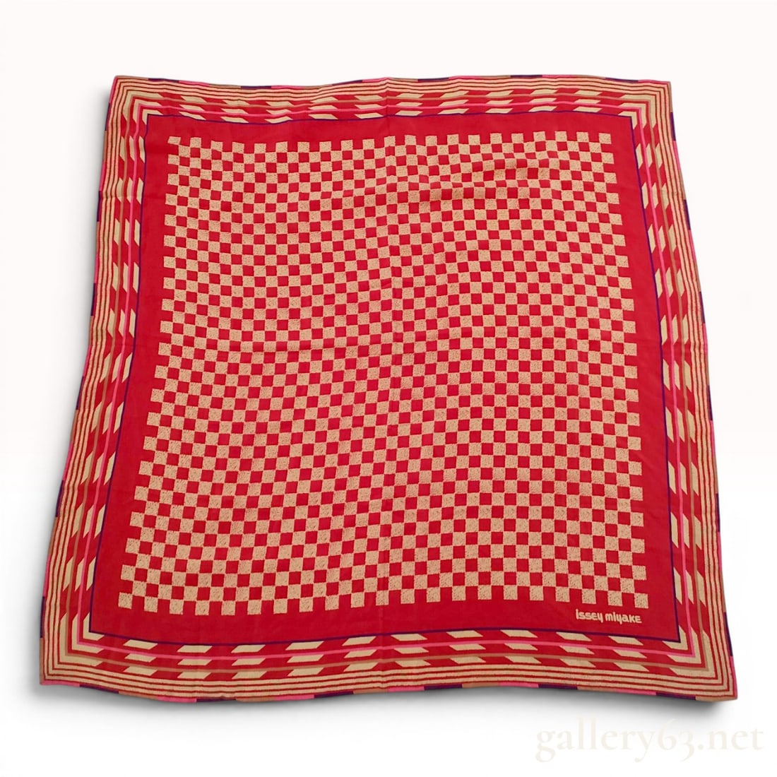 Issey Miyake Red and Cream Geometric Checkerboard Square Scarf: This Issey Miyake square scarf features a central field with a red and textured cream checkerboard pattern. The field is framed by several concentric borders in shades of purple, dark pink, and tan. T