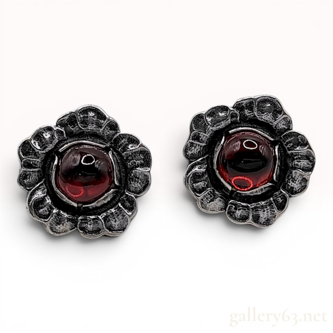 A Pair of Georg Jensen 2002 Heritage Collection Sterling Silver and Garnet Clip-On Earrings: A matched pair of sterling silver clip-on earrings by Georg Jensen, part of the 2002 annual Heritage collection. Each earring is crafted in a stylized floral motif, featuring layered and textured peta
