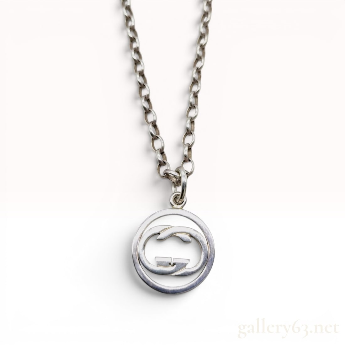 Gucci Sterling Silver Interlocking GG Logo Pendant Necklace: This is a sterling silver pendant necklace manufactured by Gucci. The piece features a rolo style chain composed of round links. Attached to the chain is a circular pendant containing a cut-out interl