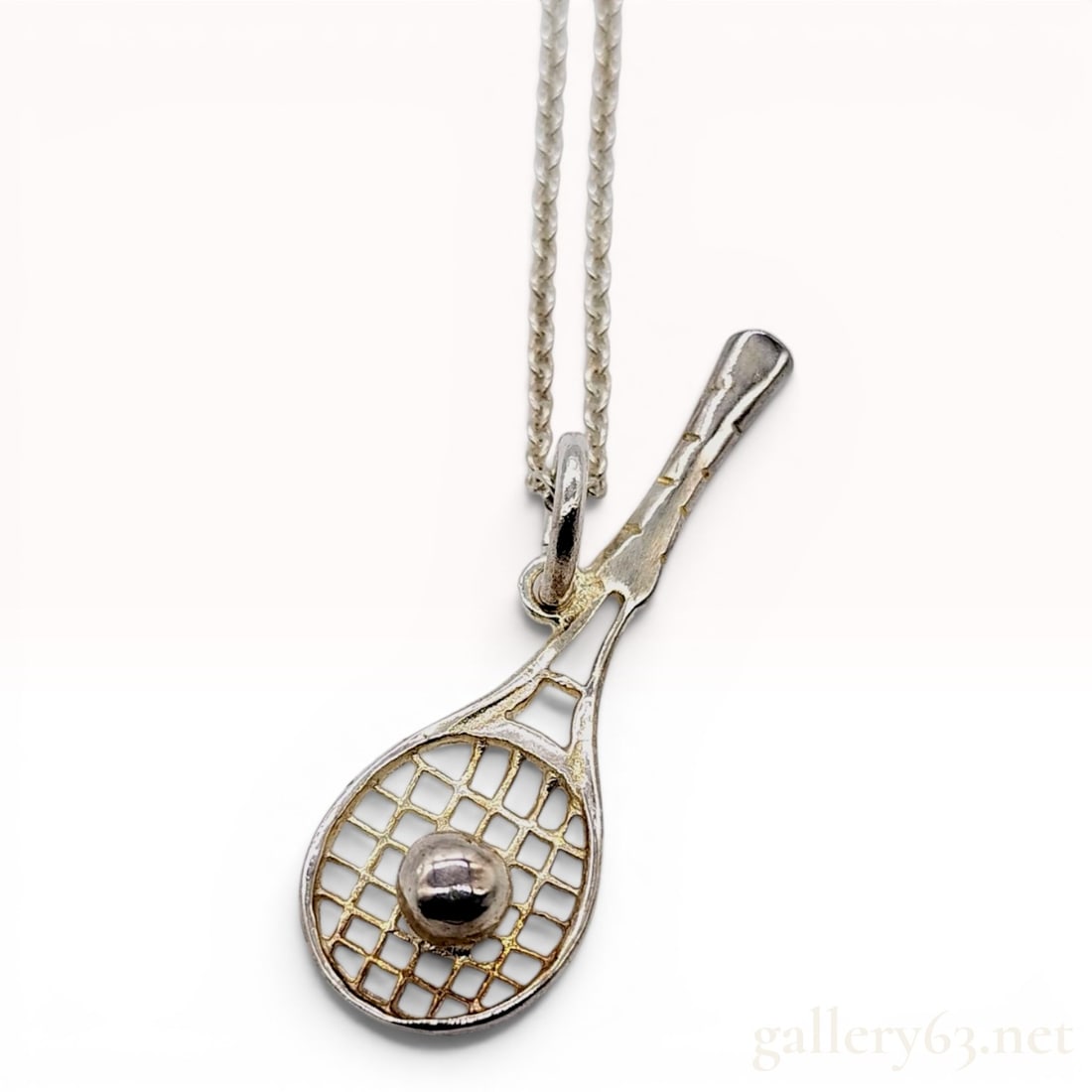 Tiffany and Co. Sterling Silver Tennis Racket and Ball Necklace: A sterling silver necklace produced by Tiffany and Co. featuring a pendant designed as a tennis racket. The pendant incorporates a three-dimensional tennis ball set within the racket strings and featu