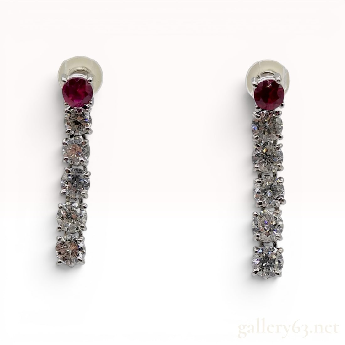 A Pair of Platinum and 1.60ctw Diamond Drop Earrings: A pair of platinum drop earrings, each featuring a round-cut reddish-pink sapphire prong-set at the top of a vertical dangle consisting of five round-cut diamonds. The settings and posts are hallmarke