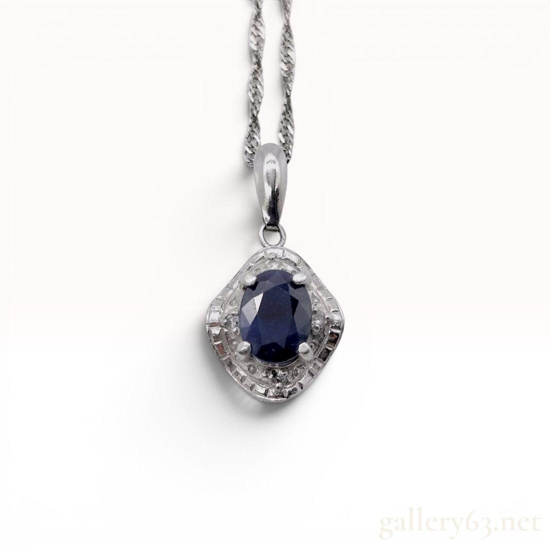 Platinum, Sapphire, and Diamond Pendant Necklace: A platinum pendant necklace featuring a shield-shaped 900 platinum pendant. The centerpiece is an oval-cut dark blue sapphire weighing approximately 1.00 carat as indicated by the stamp, secured in a 