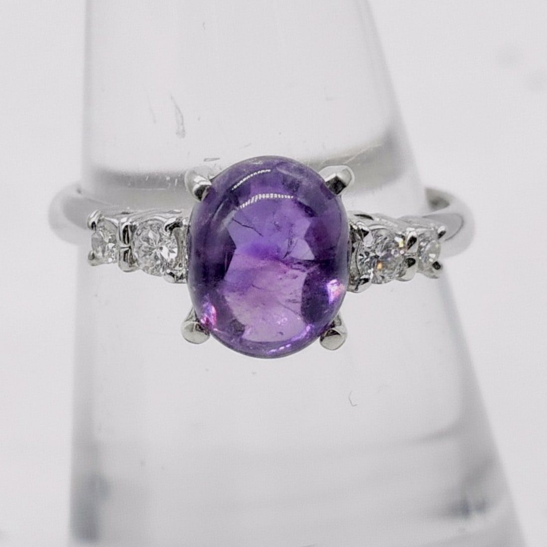 Platinum Amethyst and Diamond Dress Ring: A platinum dress ring featuring a central oval cabochon-cut amethyst secured in a four-prong setting. The shoulders are accented with a total of six round brilliant-cut diamonds, three on each side, t