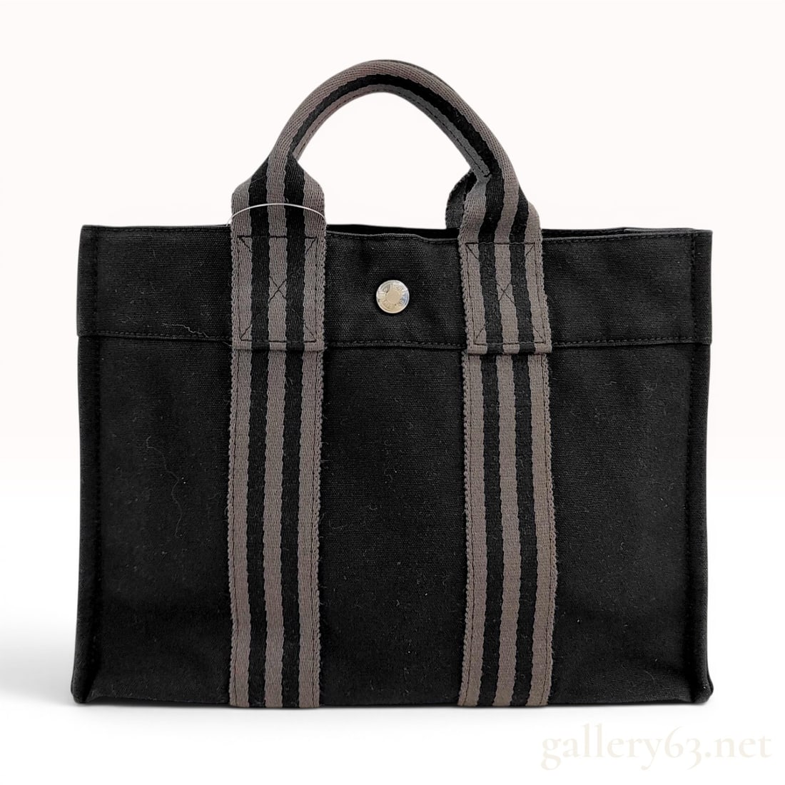 Hermes Black Canvas Fourre-Tout PM Tote Bag: This Hermes Fourre-Tout PM (Petit Modele) tote bag is constructed from durable black canvas. The design features signature vertical striped webbing handles in grey and black that extend down the front