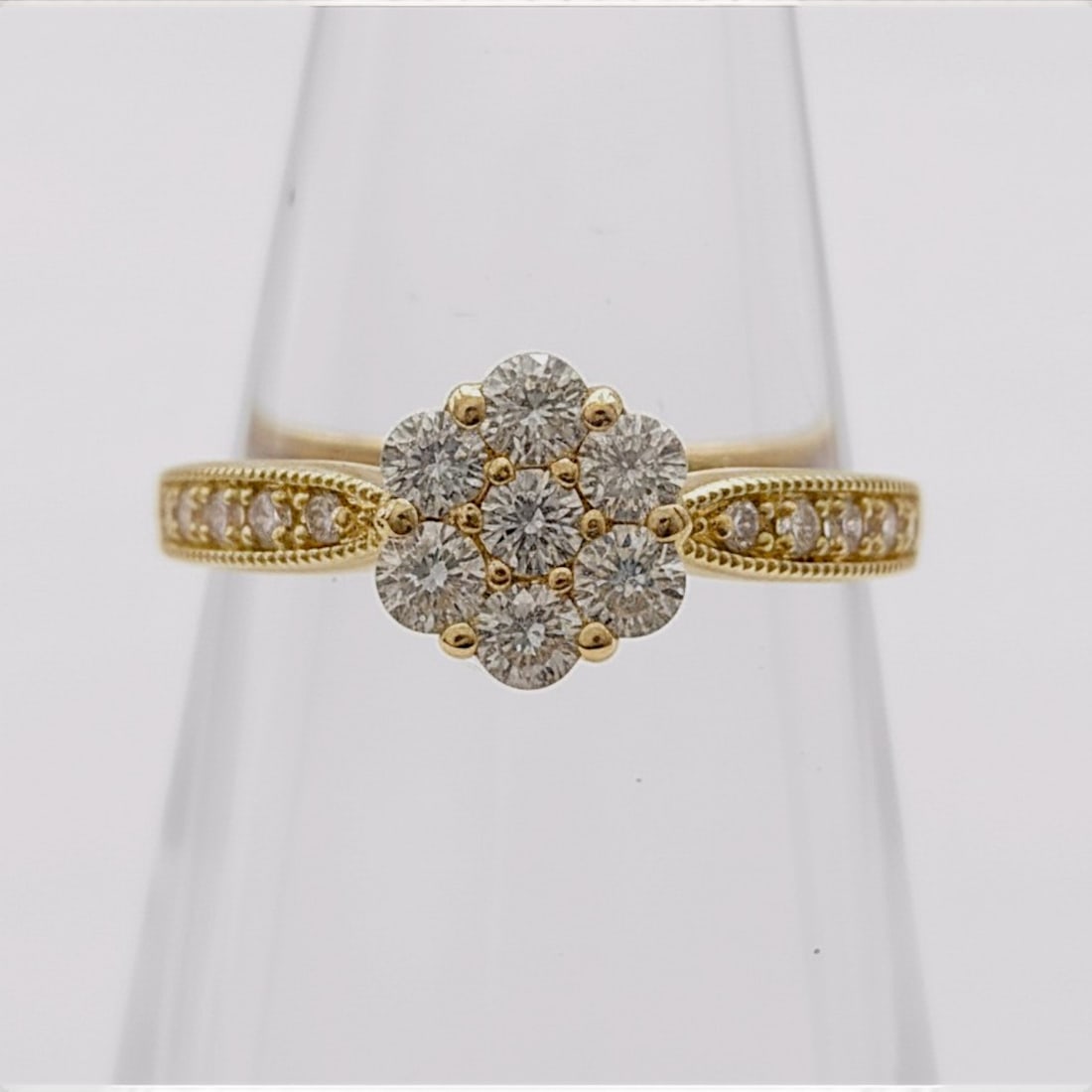 18 Karat Yellow Gold and Diamond Floral Cluster Ring: An 18 karat yellow gold ring featuring a central floral-motif cluster. The head is set with seven round brilliant-cut diamonds in a shared-prong arrangement. The tapered shoulders are accented with sm