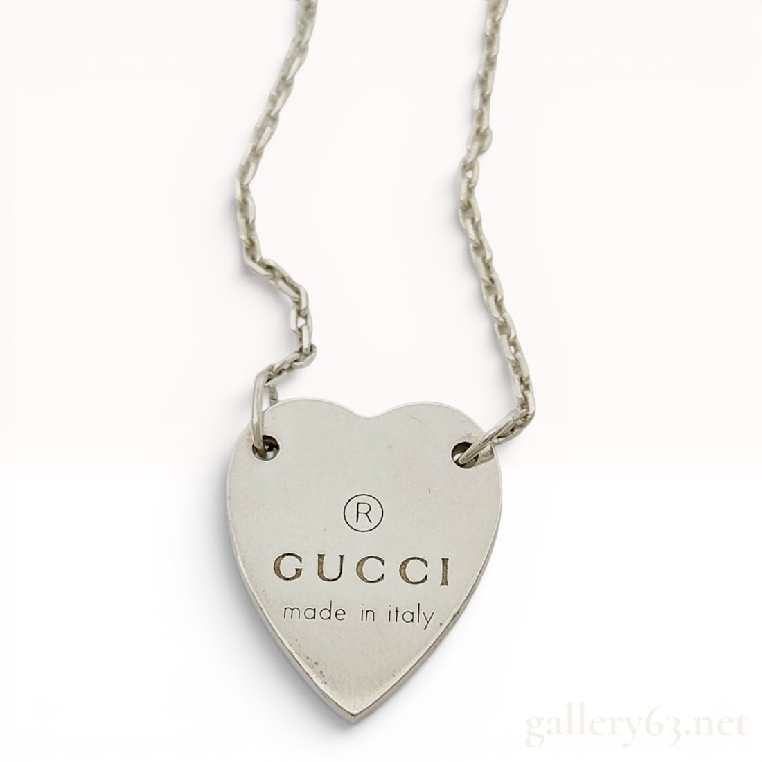 Gucci Sterling Silver Trademark Engraved Heart Pendant Necklace: A Gucci sterling silver pendant necklace from the Trademark collection. The piece features a solid heart-shaped pendant suspended from a fine cable link chain. The pendant is engraved on the front
