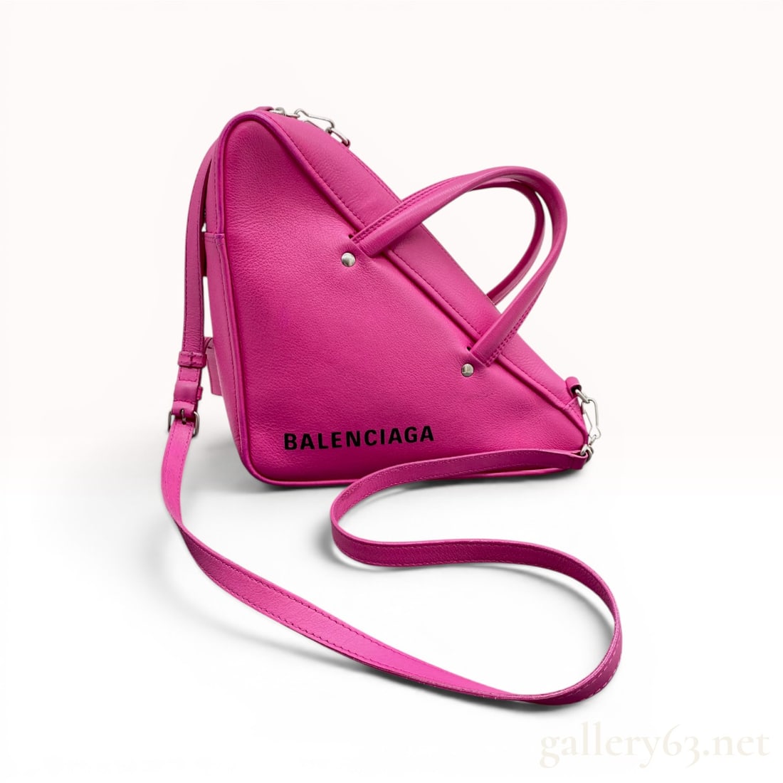 Balenciaga Pink Grained Calfskin Triangle Duffle Bag: This Balenciaga Triangle Duffle bag is crafted from pink grained calfskin leather in a distinctive triangular silhouette. The exterior features the Balenciaga logo printed in black across the front fa