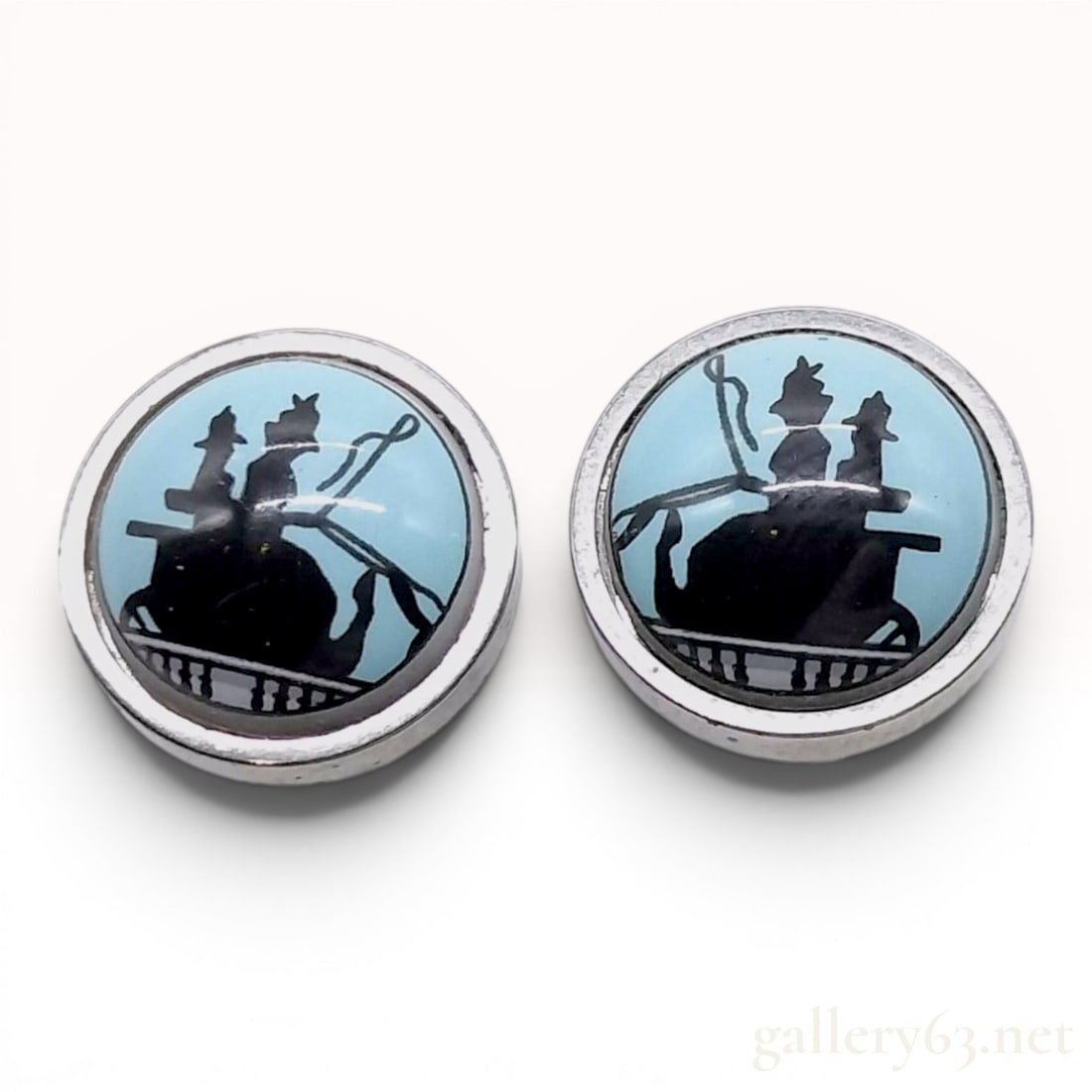 A Pair of Hermes Silver-Tone and Enamel Caleche Stud Earrings: A matched pair of stud earrings by Hermes, Paris. Each earring features a circular silver-tone metal frame bezel-set with a light blue enamel plaque. The center of each plaque is decorated with a blac