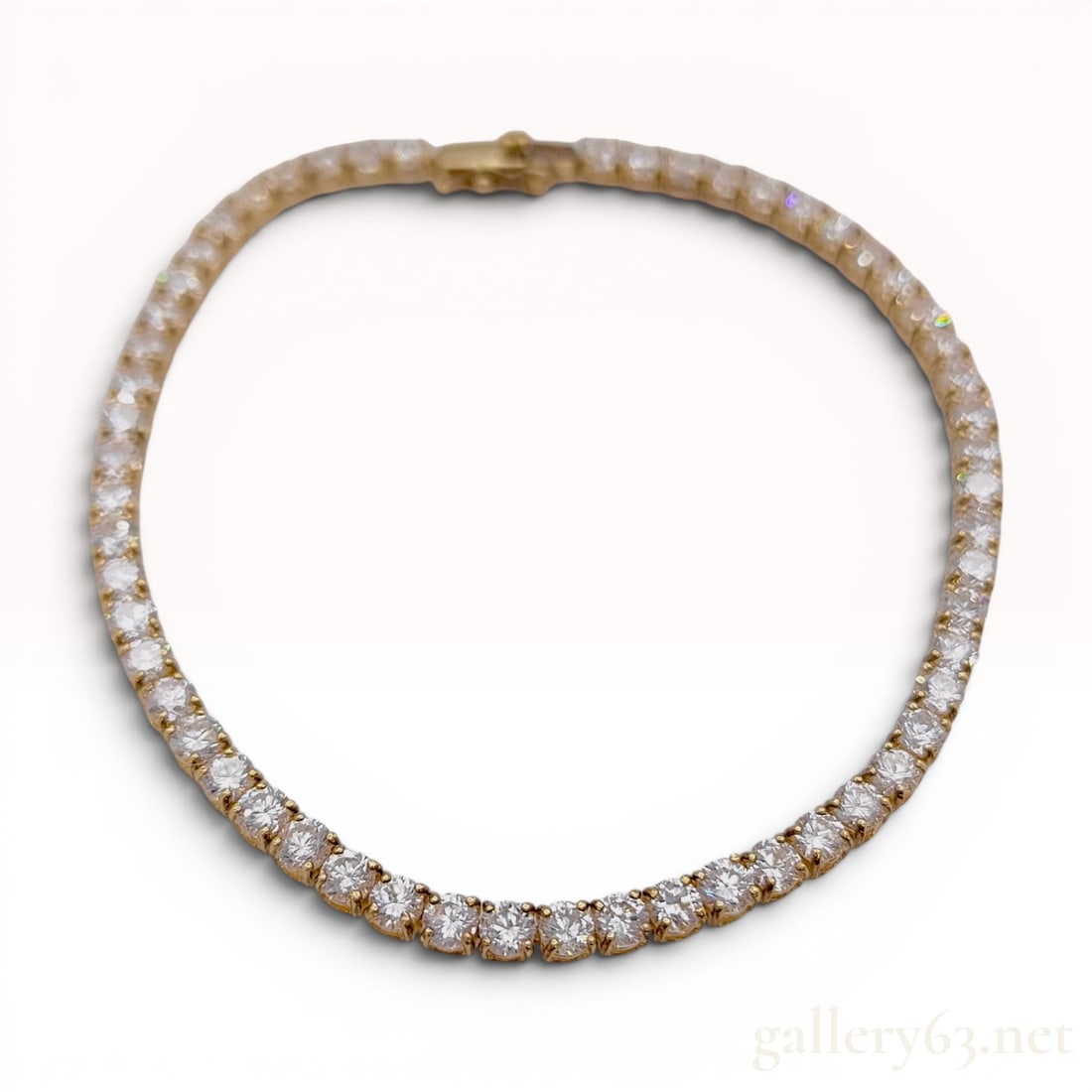 18 Karat Yellow Gold and Colorless Stone Tennis Bracelet: This tennis bracelet is crafted from 18 karat yellow gold and features a continuous row of round brilliant-cut colorless stones. Each stone is individually set in a four-prong mount with an open galle