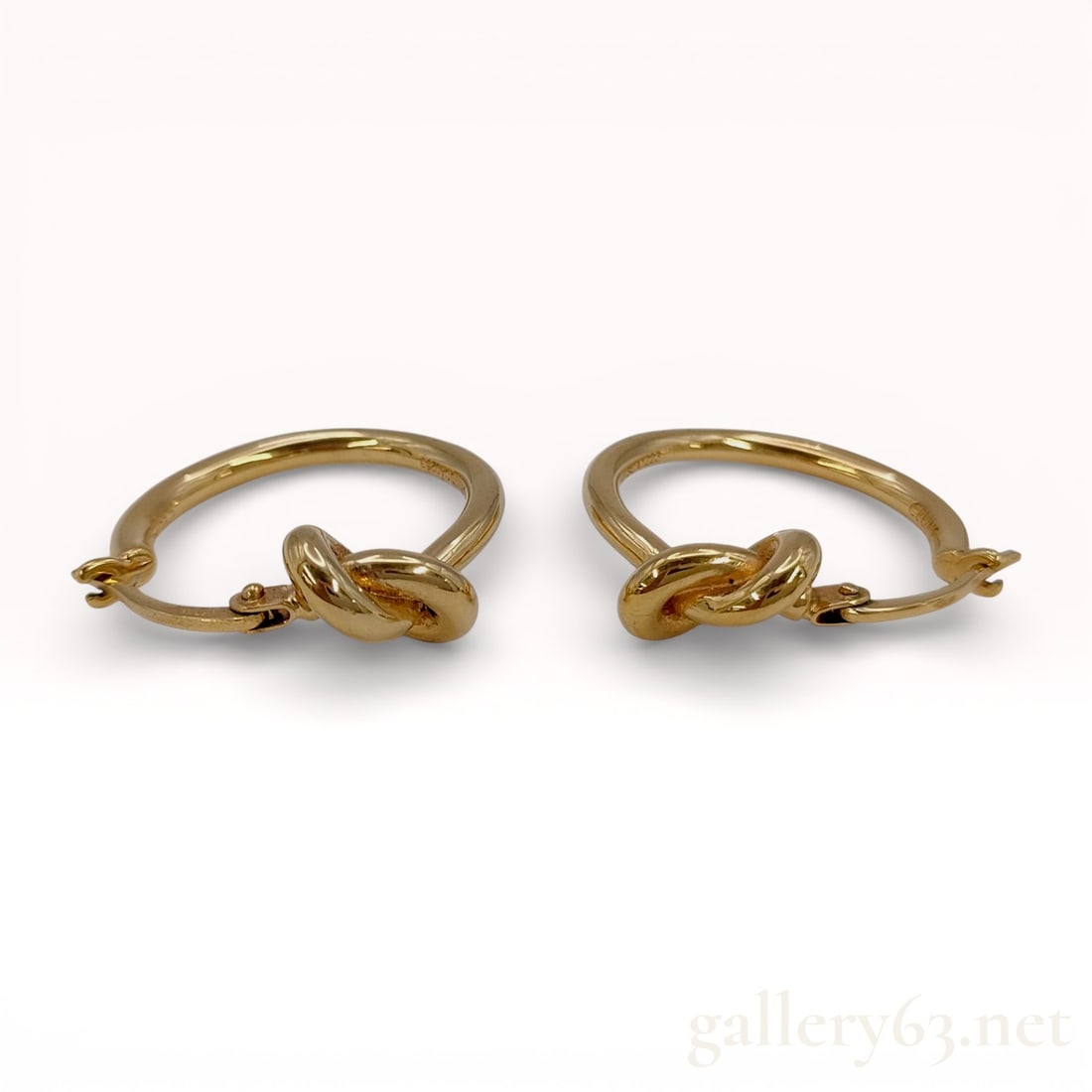 Celine Knot Small Hoops in Brass with Gold Finish: Celine Knot Small Hoops in brass with a gold finish, contemporary. This matched pair of earrings features a central overhand knot motif integrated into a hoop design with hinged lever-back closures. T