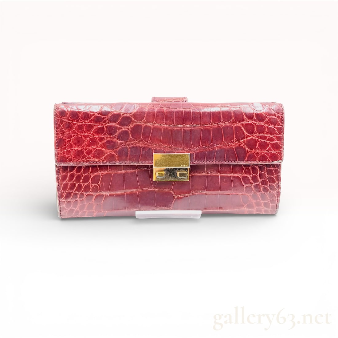 Gucci Burgundy Crocodile Skin Long Wallet: This Gucci long wallet is constructed from burgundy exotic skin featuring a rectangular scale pattern. The exterior is secured by a gold-tone metal push-lock clasp stamped with the Gucci brand name. T