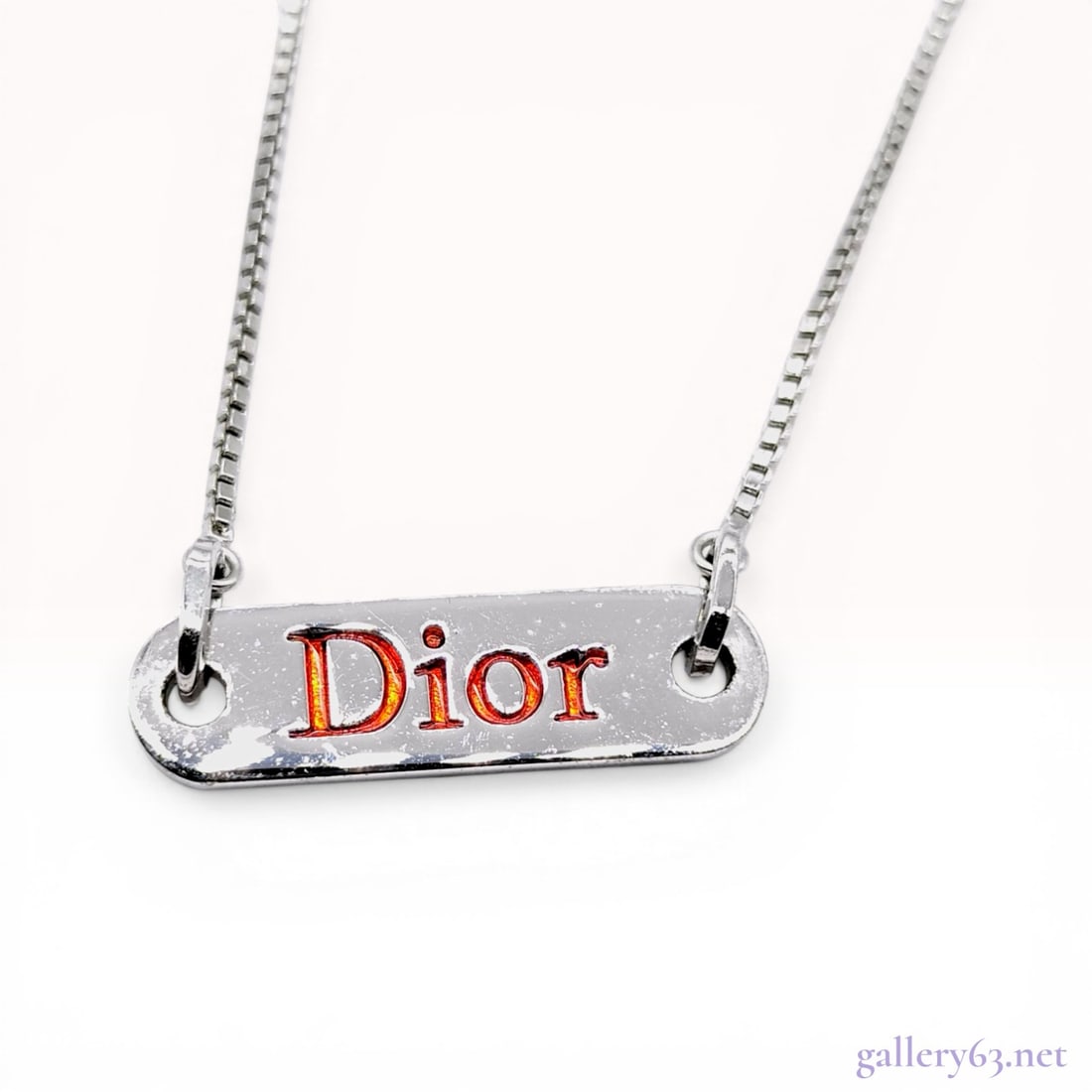 Dior Silver-Tone Logo Plate Necklace with Red Enamel: Dior costume necklace featuring a rectangular silver-tone bar pendant with raised lettering filled in red enamel. The pendant is suspended from a box-style chain with a lobster claw clasp, a D-shaped 