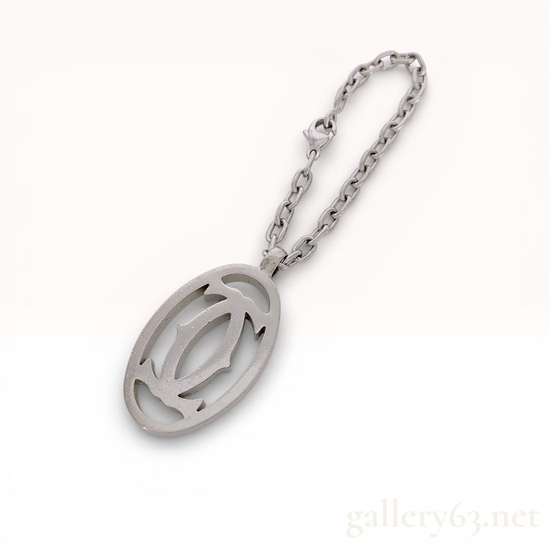 Cartier C de Cartier Logo Pendant Charm on Cable Link Chain: Cartier logo pendant charm featuring an oval openwork design with the stylized double C motif. The silver-tone metal piece is suspended from a short cable link chain with a lobster claw clasp. The sid